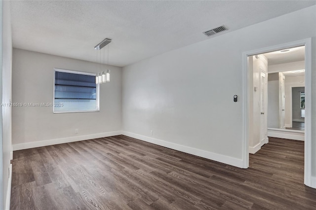 spare room with a textured ceiling, dark wood finished floors, visible vents, and baseboards