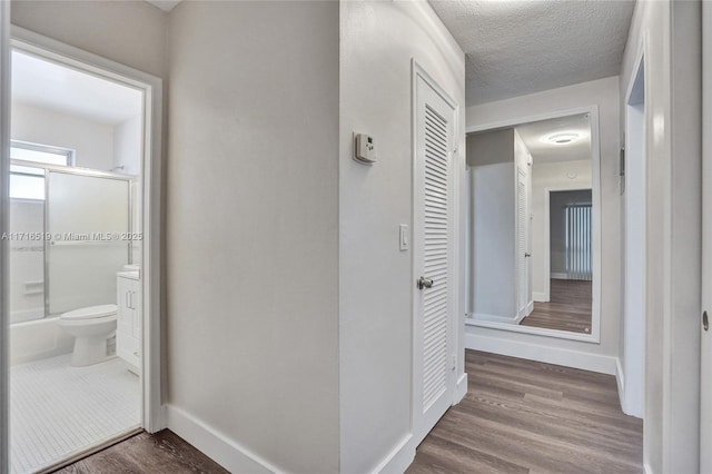 hall with a textured ceiling, baseboards, and wood finished floors