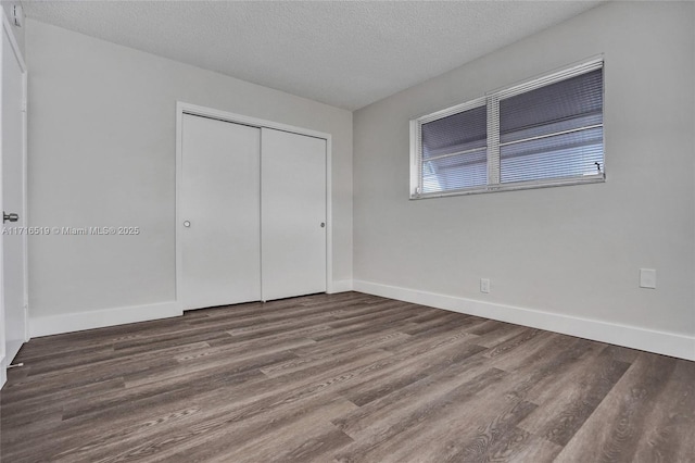 unfurnished bedroom with a closet, a textured ceiling, baseboards, and wood finished floors