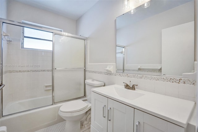 full bathroom with enclosed tub / shower combo, toilet, vanity, tile walls, and wainscoting