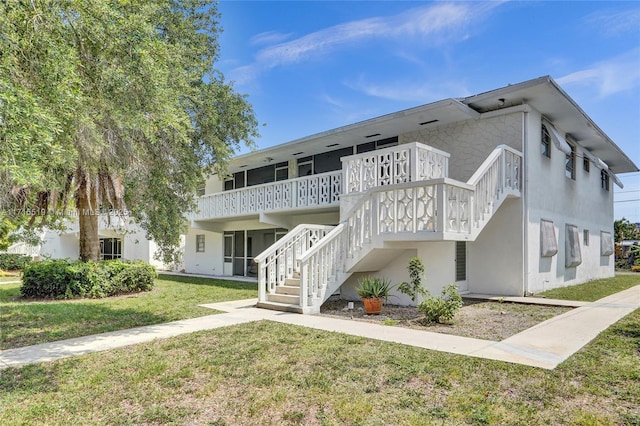 view of front of property featuring a wooden deck, stairway, a front lawn, and stucco siding