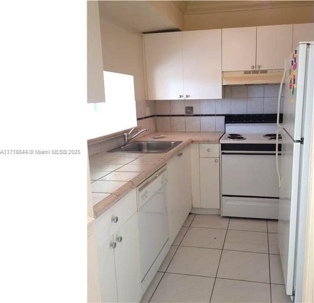 kitchen featuring white appliances, white cabinetry, decorative backsplash, sink, and light tile patterned floors