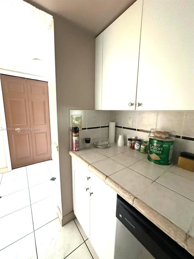 kitchen featuring stainless steel dishwasher, backsplash, tile countertops, and white cabinetry