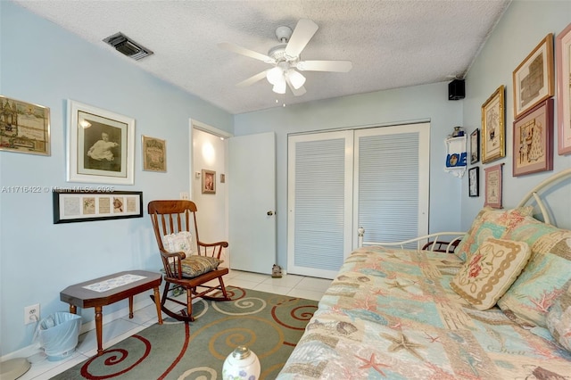 bedroom with ceiling fan, light tile patterned floors, a textured ceiling, and a closet