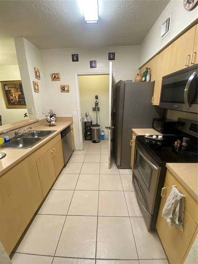 kitchen with light brown cabinets, sink, a textured ceiling, and appliances with stainless steel finishes