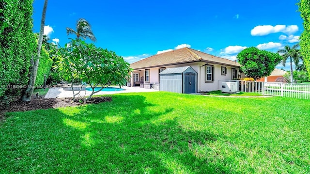 rear view of property featuring a fenced in pool, a patio area, a yard, and a storage unit