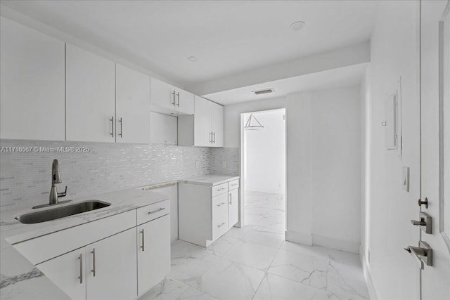 kitchen with decorative backsplash, white cabinetry, sink, and light stone counters