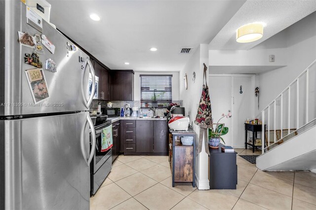 kitchen with light tile patterned floors, dark brown cabinetry, backsplash, and appliances with stainless steel finishes