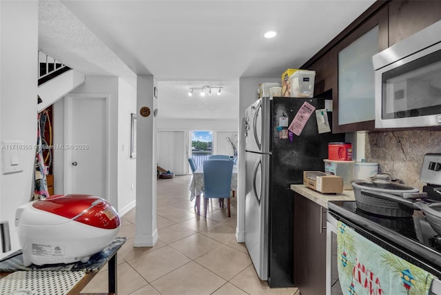 kitchen featuring light tile patterned floors, stainless steel appliances, light countertops, backsplash, and dark brown cabinetry