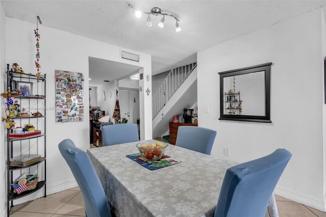 dining space with a textured ceiling, baseboards, visible vents, stairway, and light tile patterned floors