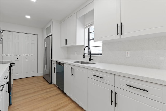 kitchen with dishwasher, sink, light wood-type flooring, white cabinetry, and stainless steel refrigerator