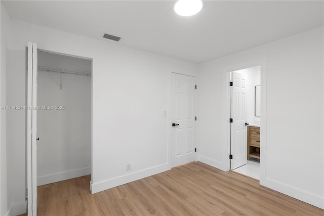 unfurnished bedroom with connected bathroom, a closet, and light hardwood / wood-style flooring