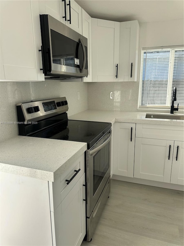 kitchen with decorative backsplash, appliances with stainless steel finishes, sink, light hardwood / wood-style flooring, and white cabinetry