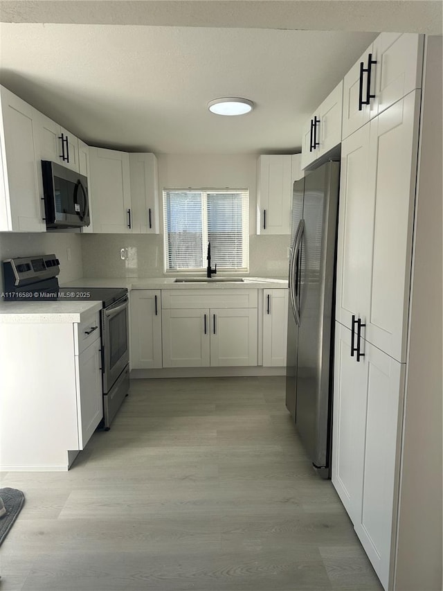 kitchen featuring white cabinets, sink, appliances with stainless steel finishes, and light hardwood / wood-style flooring