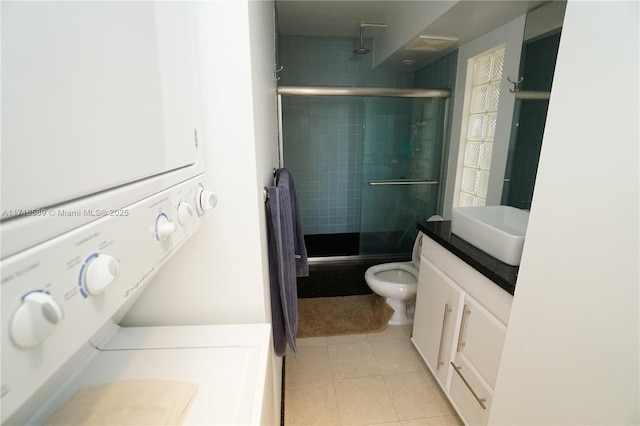 bathroom featuring toilet, vanity, stacked washing maching and dryer, a shower stall, and tile patterned floors