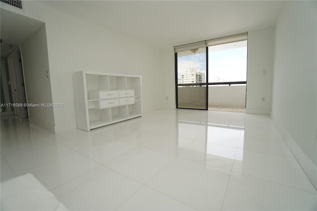 spare room with a wall of windows, tile patterned flooring, visible vents, and baseboards