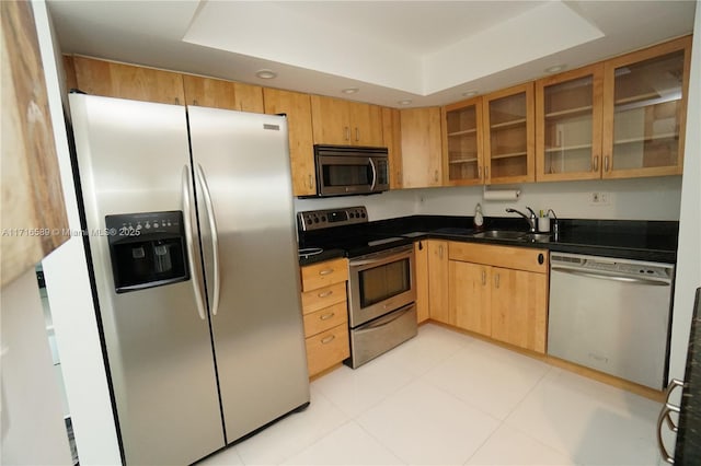 kitchen featuring stainless steel appliances, dark countertops, a raised ceiling, and a sink