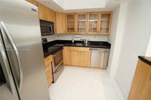 kitchen featuring stainless steel appliances, glass insert cabinets, light tile patterned flooring, a sink, and baseboards