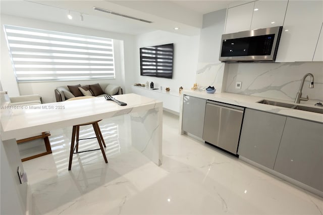 kitchen with decorative backsplash, stainless steel dishwasher, sink, white cabinets, and a breakfast bar area