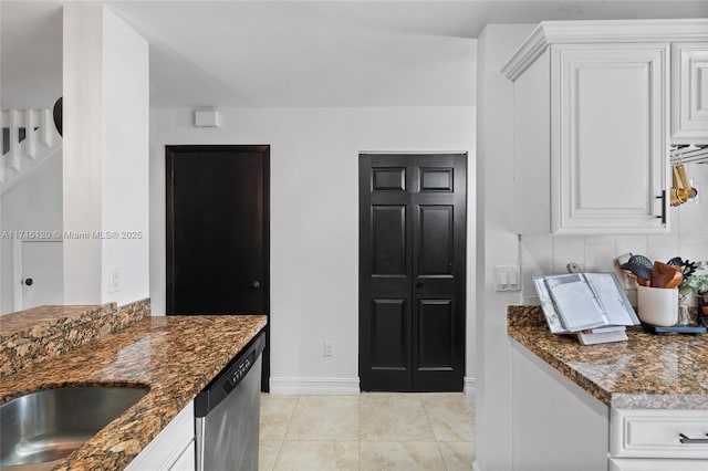 kitchen featuring white cabinets, stainless steel dishwasher, dark stone counters, and light tile patterned flooring