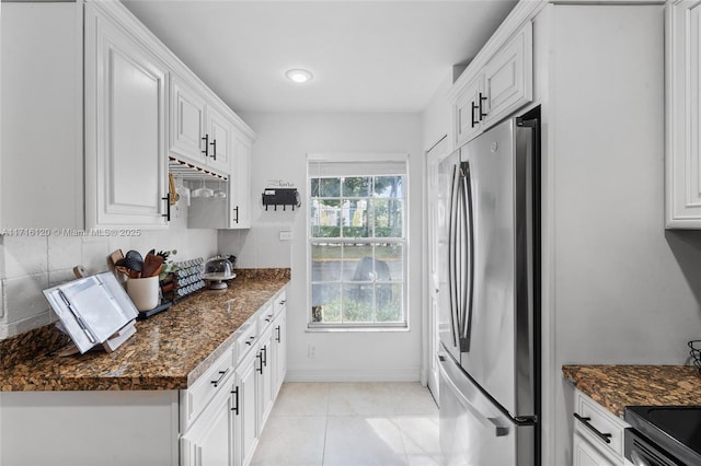 kitchen with stainless steel refrigerator, dark stone countertops, white cabinets, and light tile patterned flooring