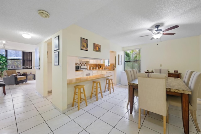 dining area featuring ceiling fan, light tile patterned flooring, and a textured ceiling