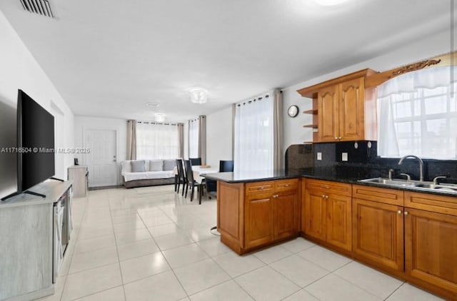 kitchen featuring sink, tasteful backsplash, kitchen peninsula, dark stone countertops, and light tile patterned floors