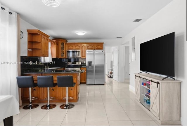 kitchen with a kitchen breakfast bar, sink, decorative backsplash, light tile patterned floors, and appliances with stainless steel finishes