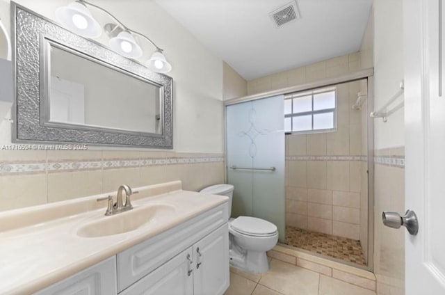 bathroom featuring vanity, tile patterned flooring, toilet, tile walls, and a shower with shower door