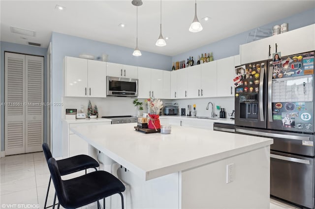 kitchen featuring pendant lighting, a kitchen breakfast bar, a kitchen island, white cabinetry, and stainless steel appliances