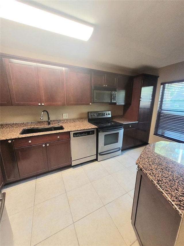 kitchen featuring sink, light stone countertops, appliances with stainless steel finishes, light tile patterned flooring, and dark brown cabinetry