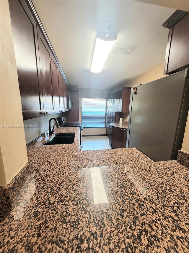 kitchen featuring dark brown cabinets, black electric range oven, sink, and dark stone counters