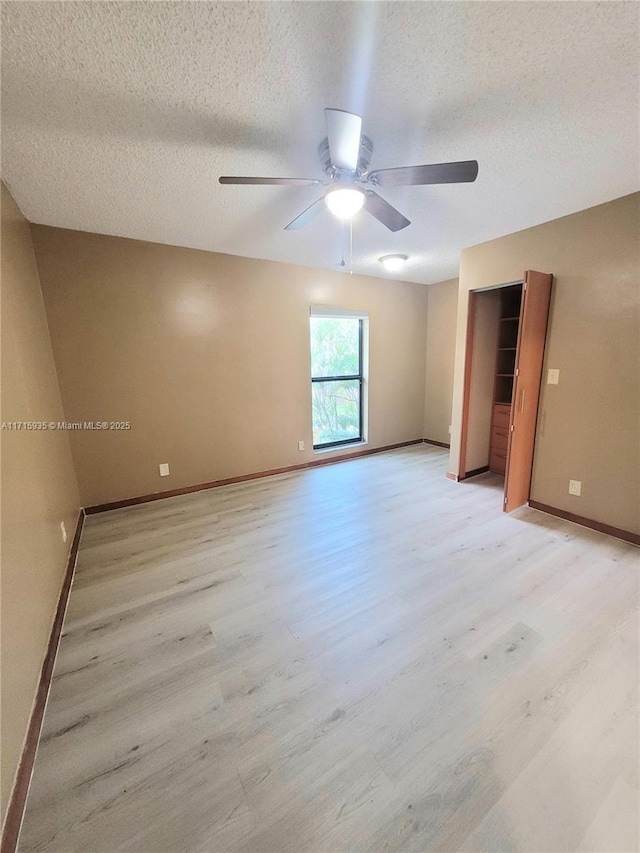 empty room with ceiling fan, light hardwood / wood-style flooring, and a textured ceiling