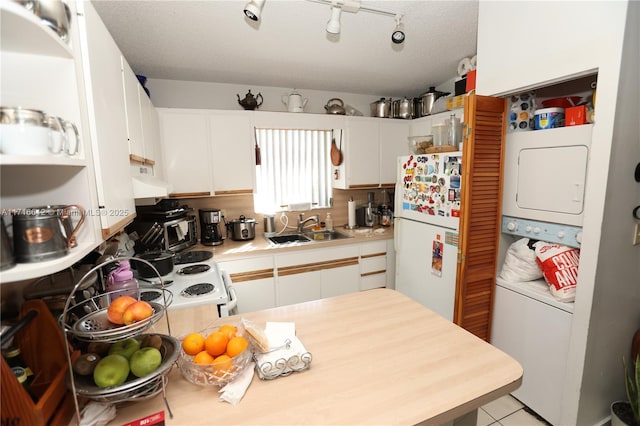 kitchen with sink, light tile patterned floors, white fridge, white cabinets, and stacked washer and dryer