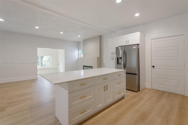 kitchen with light stone countertops, a kitchen island, stainless steel refrigerator with ice dispenser, light hardwood / wood-style floors, and white cabinets