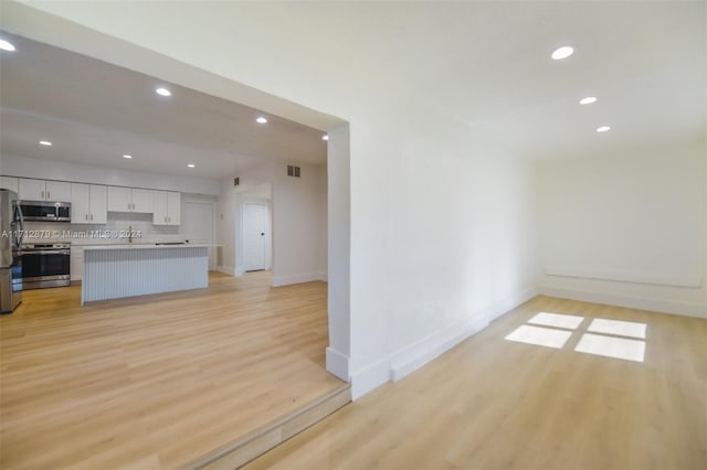 kitchen with backsplash, white cabinetry, stainless steel appliances, and light wood-type flooring