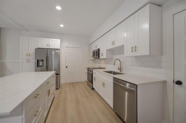 kitchen with light stone countertops, appliances with stainless steel finishes, light wood-type flooring, sink, and white cabinets