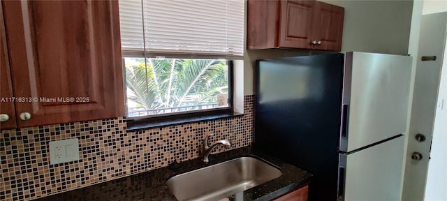 kitchen featuring backsplash, stainless steel refrigerator, sink, and dark stone countertops