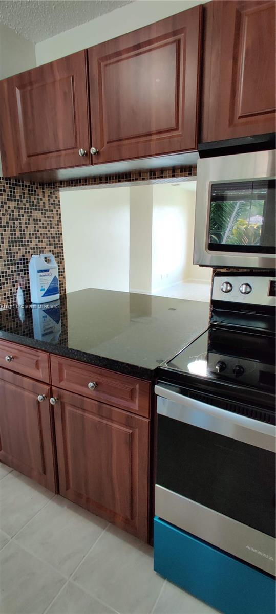 kitchen featuring tasteful backsplash, light tile patterned flooring, dark stone counters, and appliances with stainless steel finishes