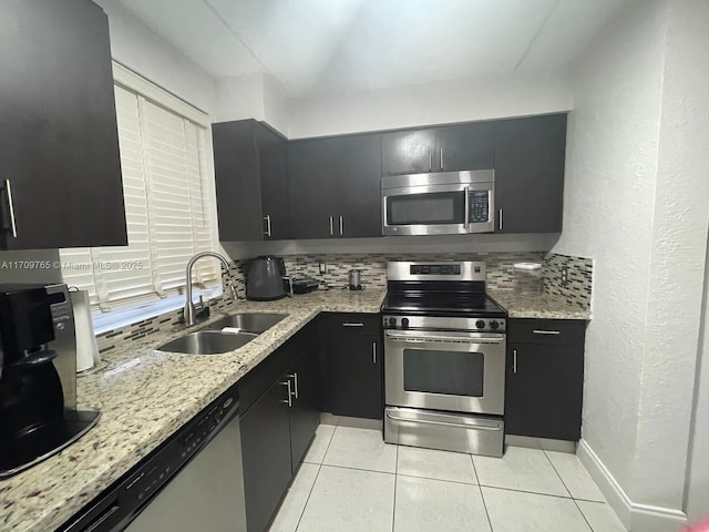 kitchen featuring light stone countertops, stainless steel appliances, sink, backsplash, and light tile patterned flooring