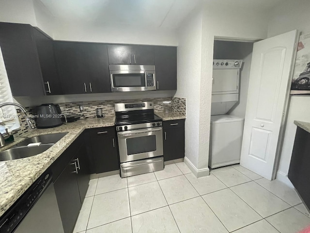 kitchen with light stone countertops, appliances with stainless steel finishes, sink, light tile patterned floors, and stacked washer and dryer