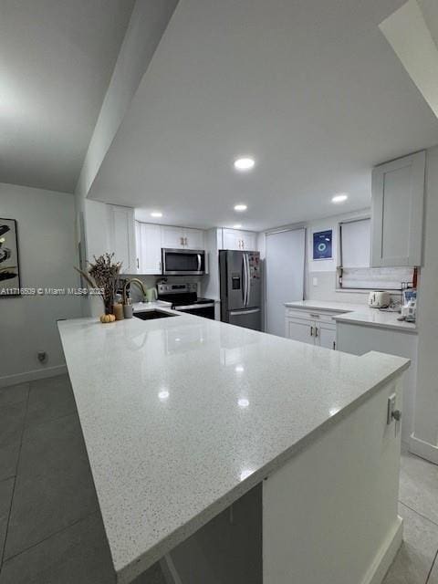 kitchen with appliances with stainless steel finishes, sink, light stone counters, and white cabinetry