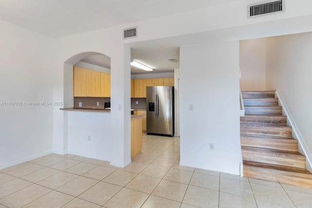 kitchen featuring kitchen peninsula, stainless steel fridge with ice dispenser, light brown cabinetry, and light tile patterned floors