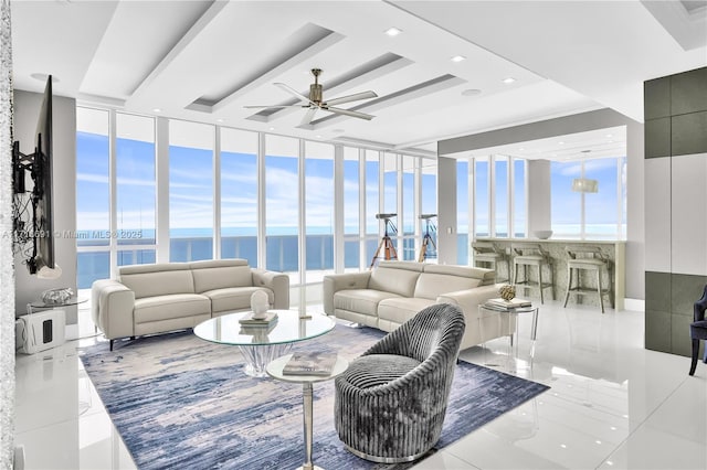 tiled living room with a tray ceiling, floor to ceiling windows, ceiling fan, and a water view