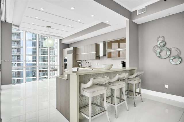 kitchen with wall chimney exhaust hood, hanging light fixtures, kitchen peninsula, a kitchen bar, and ornamental molding