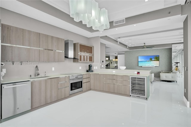 kitchen with stainless steel dishwasher, sink, wall chimney range hood, light brown cabinets, and oven