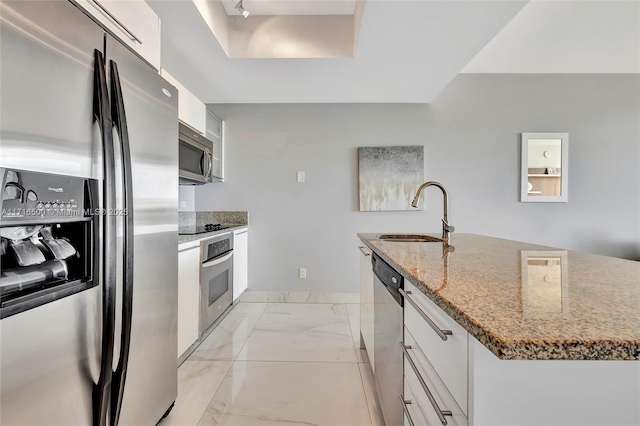 kitchen with appliances with stainless steel finishes, light stone counters, sink, a center island with sink, and white cabinetry