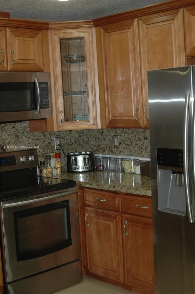 kitchen with tasteful backsplash, light stone countertops, and appliances with stainless steel finishes