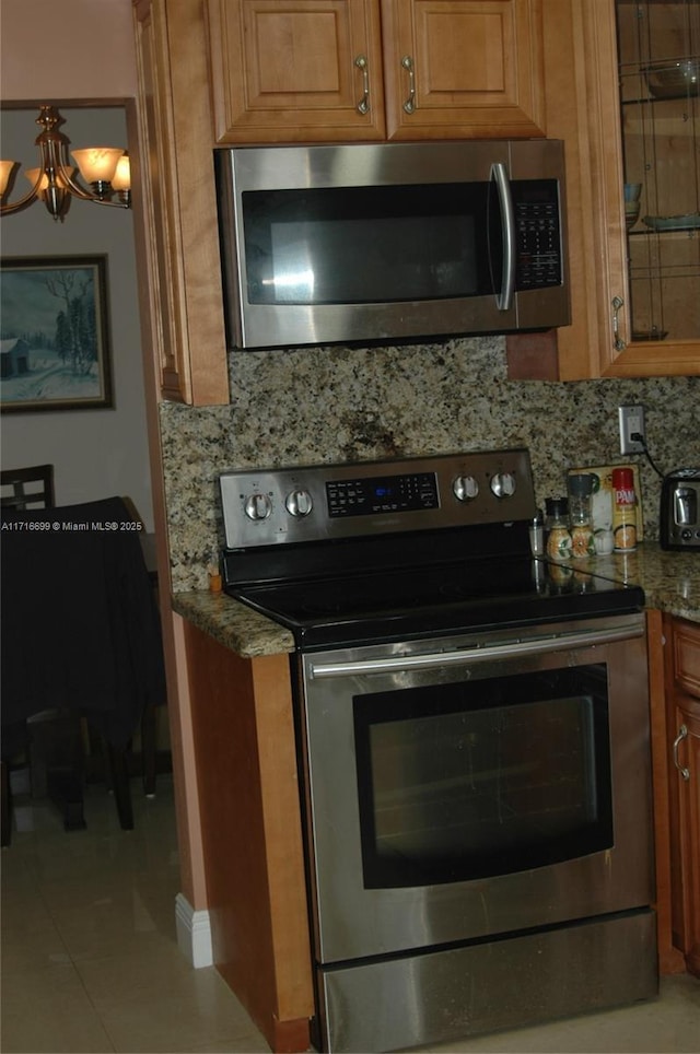 kitchen featuring appliances with stainless steel finishes, tasteful backsplash, light tile patterned floors, a notable chandelier, and stone counters