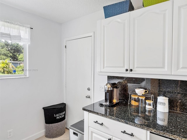 bar featuring a textured ceiling, backsplash, white cabinetry, and dark stone counters